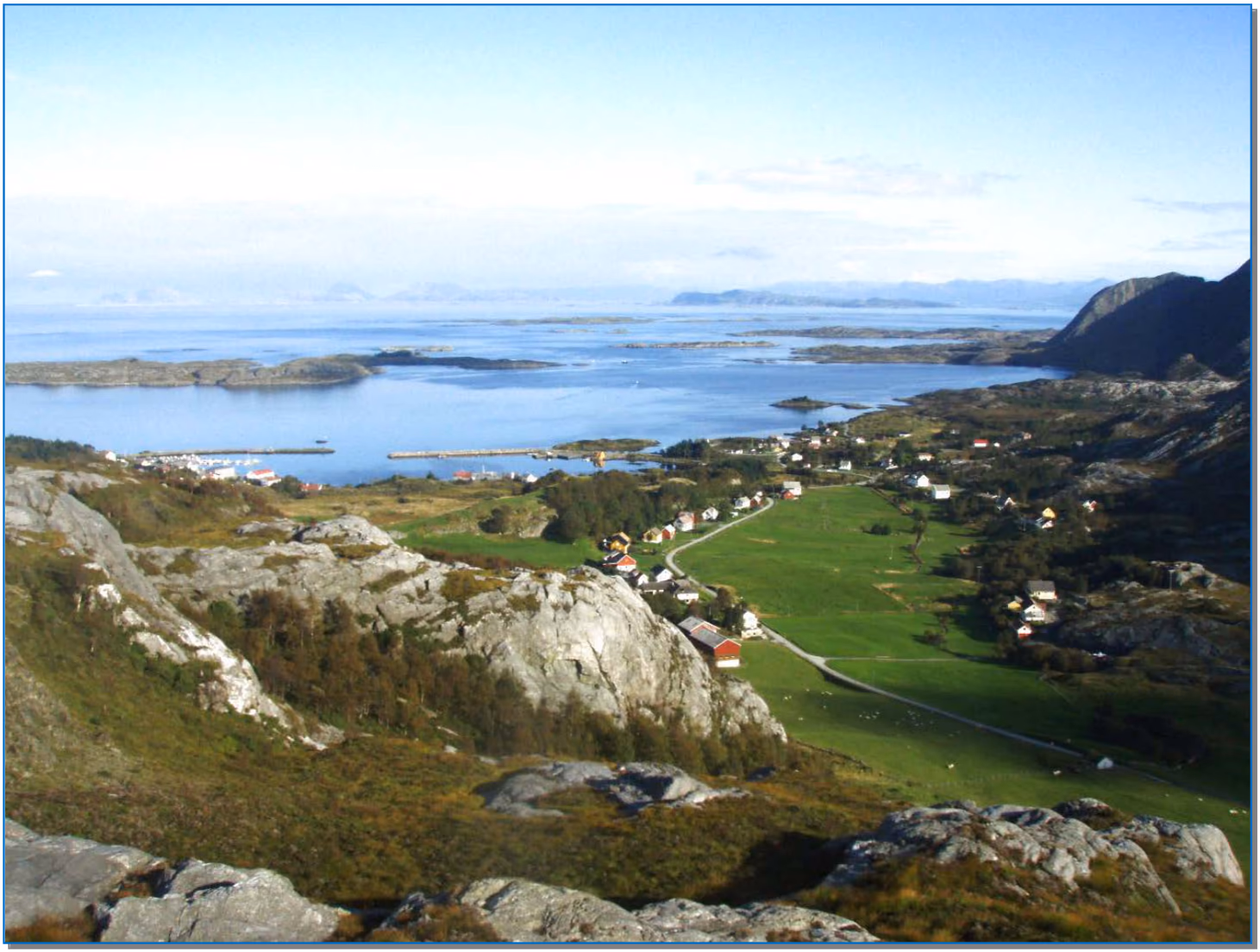 Utsikt over den nordlige delen av bygda Herland på Atløyna, med fjell, lyng, skog, dyrket mark, hus, en havn og øyer og skjær i havet